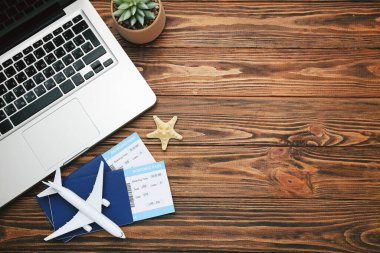Pasaportları, laptopu, uçak modeli ve ahşap arka planda deniz yıldızı olan uçak biletleri.