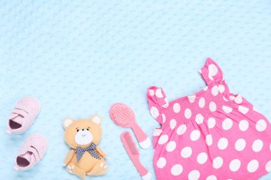 Yumuşak ayıcıklı bebek kıyafetleri ve mavi arka planda saç fırçası