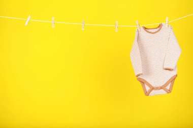 Bebek kıyafetleri sarı arka planda asılı.