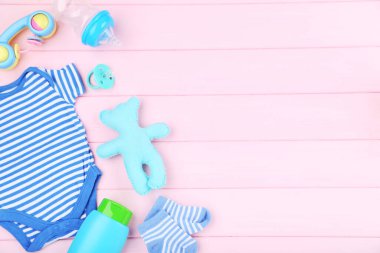 Pembe ahşap masa üzerinde oyuncaklar ve şişe ile bebek giysileri