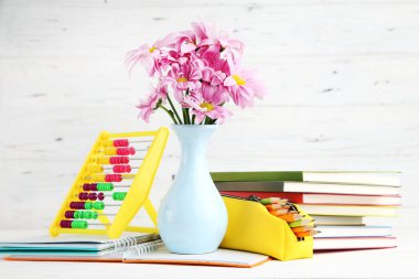 Vazoda bir buket mor kasımpatı, kalem kutusu, renkli abaküs ve beyaz ahşap arka planda not defterleri. Öğretmenler Günü