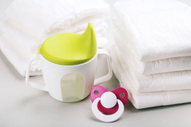 Bir bardak içkili bebek bezi ve gri arka planda emzik.