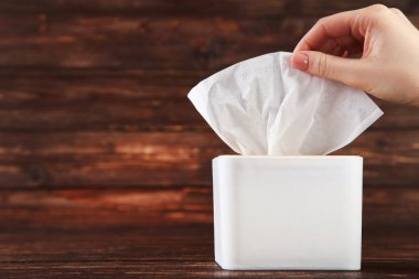 Kahverengi ahşap arka planda kadın eli olan peçete kutusu.