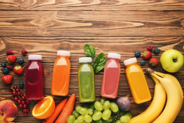 Kahverengi ahşap arka planda meyve ve sebzeli plastik şişelerde meyve püresi