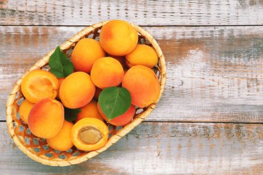 Tahta arka planda sepetinde yaprakları olan tatlı kayısılar.