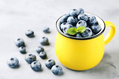 Nane yapraklı yaban mersini ve gri arka planda sarı kupa.