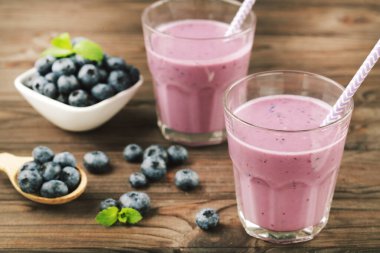 Yaban mersini ve bir bardak smoothie ve ahşap arka planda yeşil yapraklar.