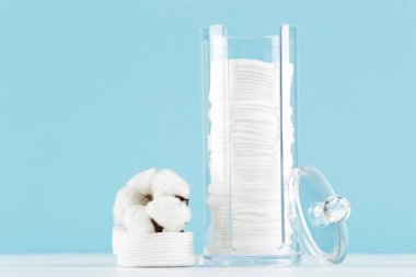 Plastik kavanozda pamuk pedler ve mavi arka planda çiçek.