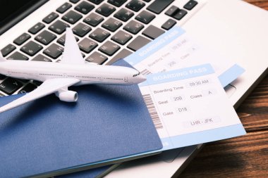 Pasaportlu, laptoplu ve ahşap arka planda uçak modelli uçuş kartları.