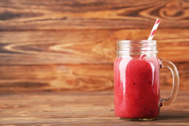 Kahverengi ahşap arka planda cam kavanozda kırmızı smoothie.