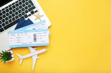 Pasaportları, laptopu, uçak modeli ve sarı arka planda yeşil fabrikası olan uçak biletleri.