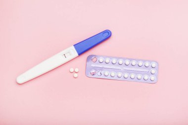 Sözlü doğum kontrol hapları ve pembe arka planda hamilelik testi.