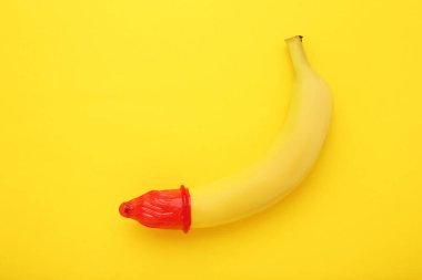 Sarı arka planda prezervatifli muz.