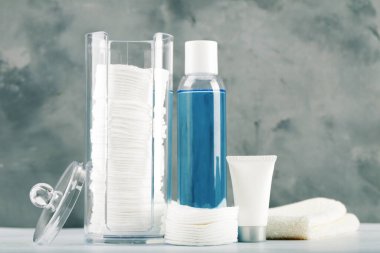 Plastik kavanozda pamuk pedler ve gri arka planda kozmetik şişeler.
