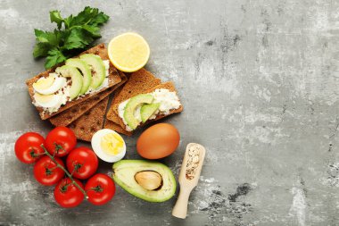 Krem peynirli çıtır ekmek, gri arka planda yumurta ve sebze.