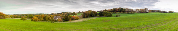 Panoramic rural autumn landscape in North Rhine Westphalia in Germany. Farm house in the middle of a huge green field.