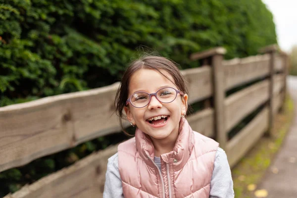 Gözlüklü, tahta çitin yanında gülen güzel bir kız. Yelekli bir köy çocuğu kırsalda yürüyüşe çıkmış.