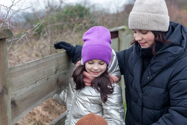 冬の服を着た母と娘が木製の柵のそばに立ってお互いを見て — ストック写真