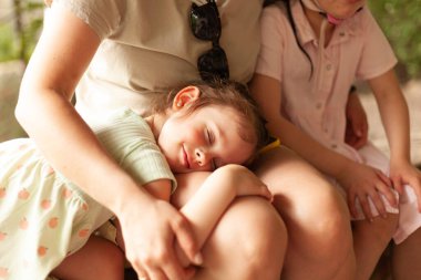 Elbiseli neşeli sarışın kız annesinin dizlerinin üstüne çöktü.