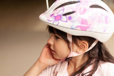 Bisiklet kasklı, küçük siyah saçlı kız bisiklet sitesinde pembe elbiseli.