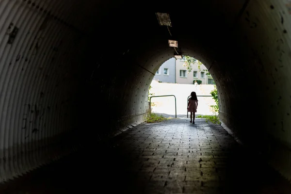 stock image Young woman walking through a tunnel in an urban environment, back view