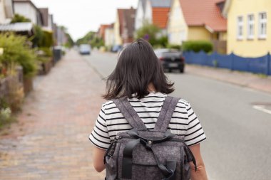 Çizgili tişörtlü ve sırt çantalı bir kız deniz kenarı şehrinin sokaklarında yürüyor. Avrupa 'da tatilde bir gezgin. Arka plan fotoğrafı