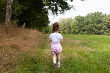 Yazın çayırda koşan küçük bir kızın arka görüntüsü.