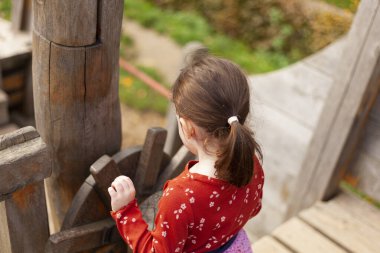 little girl in a red T-shirt plays on the playground on a pirate ship clipart