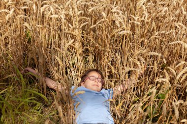 Gözlüklü, güzel bir buğday tarlasında uzanıp doğanın huzur ve güzelliğinin tadını çıkaran küçük bir kızın huzurlu ve neşeli anının özü.