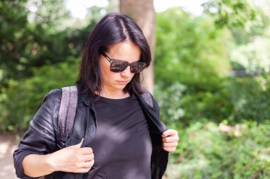 Genç bir kadın ormanda yürüyor, siyah elbiseler ve güneş gözlüğü takıyor..