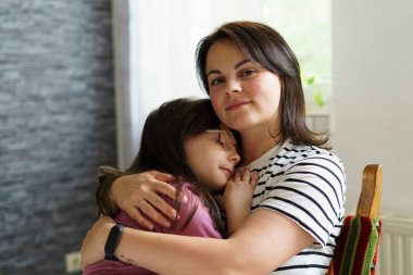 Anne ve kızı oturma odasında birbirlerine sarılıyorlar..