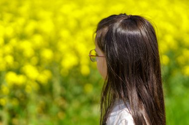 Sarı çiçek tarlasında gözlüklü genç kız. Seçici odak.
