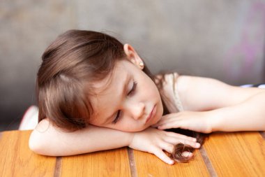 Küçük üzgün kız yazın bir sokak kafesinde ahşap bir masada uyuyor.