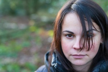 Close-up portrait of a beautiful dark-haired girl in a black jacket and backpack standing in the forest clipart