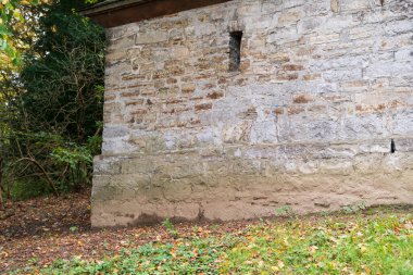 Sonbahar parkında küçük pencereli eski bir taş bina.