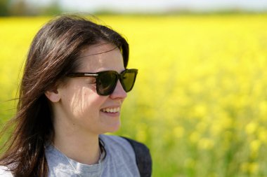 Güneş gözlüklü genç bir kadın çiçek açan bir kolza tohumu tarlasında.