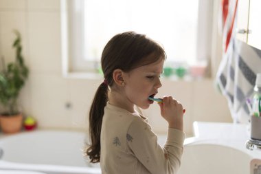 Atkuyruklu tatlı bir kız pencerenin karşısındaki banyoda dişlerini fırçalıyor. Tıbbi diş konsepti.