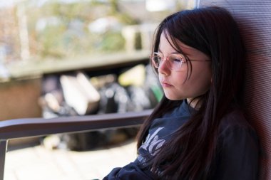 Koyu renk saçlı, gözlüklü, arka bahçedeki masada oturan kız. Tatlı çocukların zorlukları konsepti