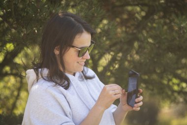Gülümseyen, tatlı, koyu renk saçlı bir kız evinin arka bahçesinde otururken cep telefonuyla bir video görüşmesinde konuşuyor. Aile ile iletişim teknolojisi kavramı