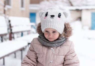 Örgü şapkalı ve kışın açık havada sıcak giysileri olan küçük, gücenmiş bir kız. Karda çocuk oyunları