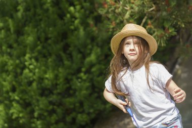 Uzun saçlı, uzun saçlı, hasır şapka takan tatlı bir kız yaz bahçesinde badminton oynuyor.