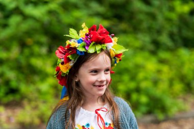 Ukrayna çiçekli çelenk ve geleneksel işlemeli bluz giyen mutlu küçük bir kız yazın dışarıda dururken neşe saçıyor..