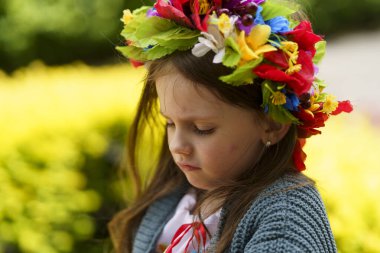 A young girl, donning a Ukrainian floral wreath, appears disheartened on a sunny summer afternoon. clipart