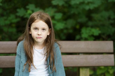 Üzgün, güzel, dişsiz, kızıl saçlı kız dışarıdaki ahşap bir bankta oturuyor. Çocukların hüzünlü seyahat konsepti