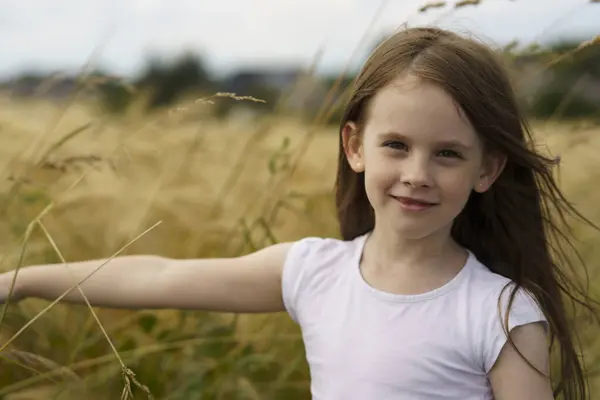 stock image Cute beautiful little toothless red-haired girl against the background of a wheat field and a rural road. Children's travel concept