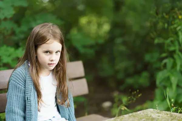 Stock image Sad beautiful little toothless red-haired girl sits on a wooden bench outdoors. Sad children's travel concept