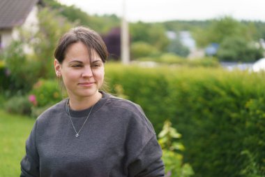 Genç, gülümseyen, saçları toplayan ve yazın arka bahçede kazak giyen güzel bir kız. Mutlu bekar yaşam konsepti