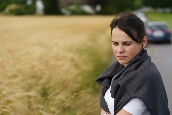 stock image A young smiling beautiful girl with collected hair and a sweater thrown over her shoulders against the backdrop of a field with ripe wheat. Rural travel or farming concept