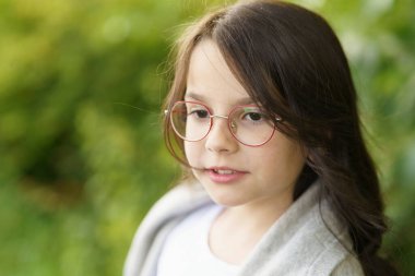 Gözlüklü, kot pantolonlu, tişörtlü ve omuzlarına kazak geçirilmiş genç bir kız beline kadar otların arasında duruyor. Yaban çiçeklerinde biraz çocuksu mutluluk.