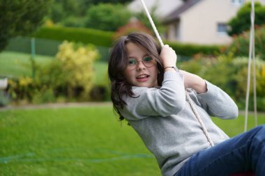 Kıvırcık saçlı gözlüklü bir kız yazın arka bahçede salıncakta sallanıyor. Mutlu çocukluk kavramı.